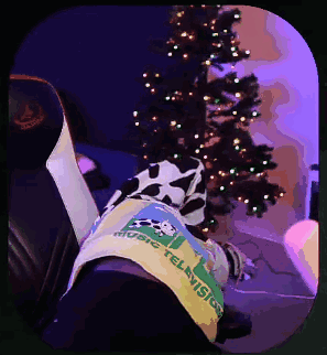 A Person Wearing A Shirt That Says Music Television Is Laying In Front Of A Christmas Tree GIF