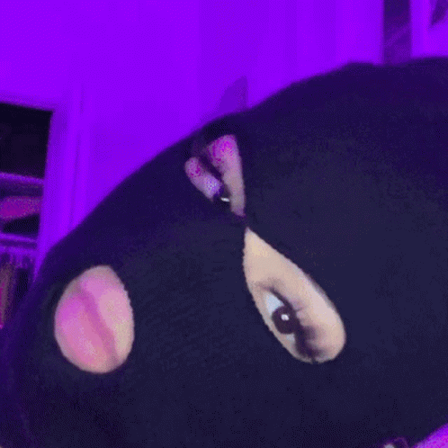 A Person Wearing A Ski Mask With Holes In It Is Standing In Front Of A Purple Wall GIF
