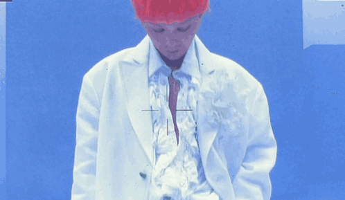 A Person Wearing A White Jacket And A Red Hat Stands In Front Of A Blue Background GIF