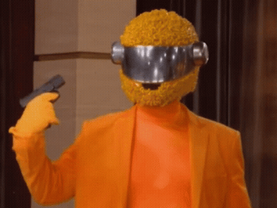 A Person Wearing An Orange Suit And A Yellow Helmet Is Holding A Gun To Their Head GIF