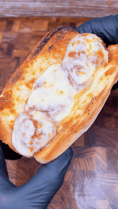 A Person Wearing Black Gloves Is Holding A Meatball Sub With Cheese GIF