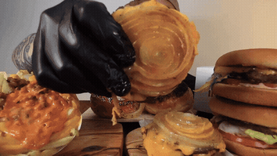 A Person Wearing Black Gloves Is Holding A Piece Of Cheese On A Hamburger GIF