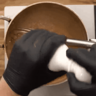 A Person Wearing Black Gloves Is Mixing Something In A Pot With A Blender . GIF