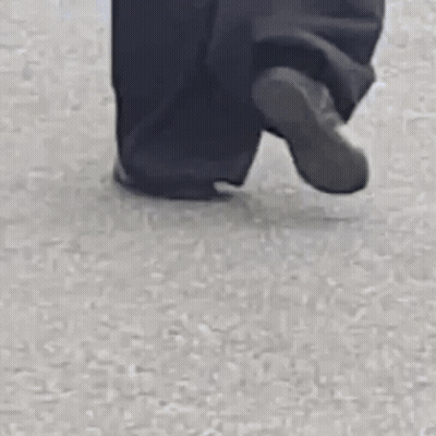A Person Wearing Black Pants And A White Jacket Is Walking On A Street . GIF