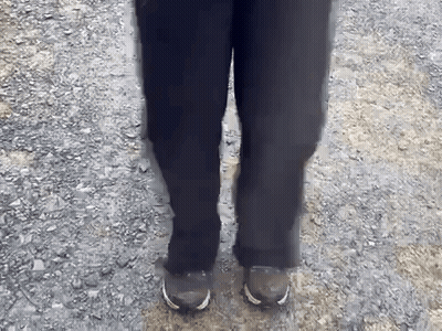 A Person Wearing Black Pants And Brown Shoes Is Standing On A Gravel Path GIF