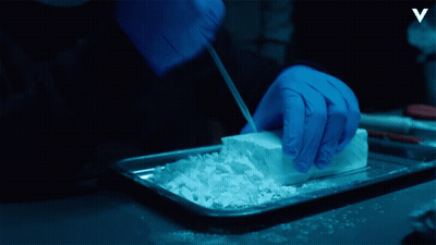 A Person Wearing Blue Gloves Is Cutting Up A Piece Of White Powder GIF