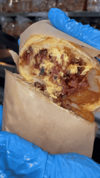A Person Wearing Blue Gloves Is Holding A Burrito With Meat And Eggs GIF
