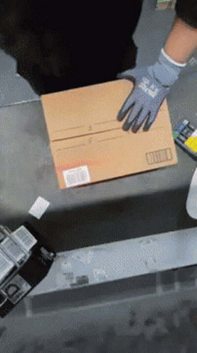 A Person Wearing Gloves Is Holding A Cardboard Box With A Barcode On It GIF