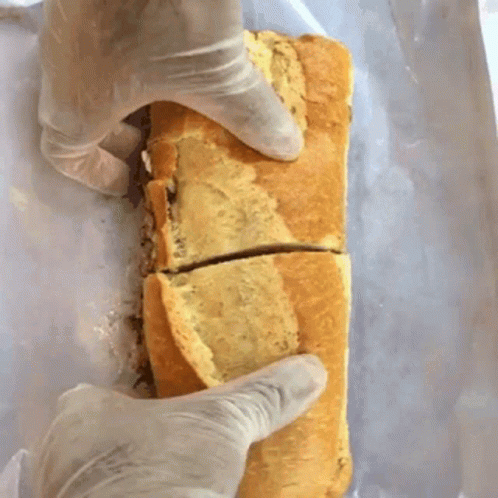 A Person Wearing Gloves Is Holding A Sandwich That Has Been Cut In Half GIF