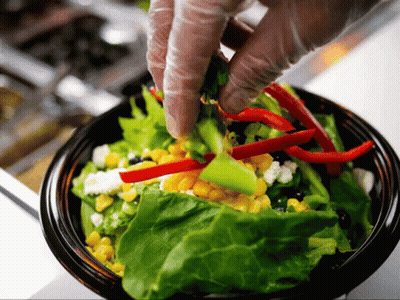 A Person Wearing Gloves Is Putting Vegetables Into A Salad GIF