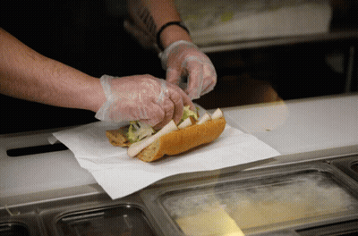 A Person Wearing Plastic Gloves Prepares A Sandwich GIF