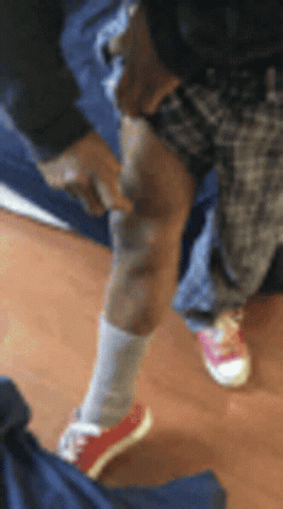 A Person Wearing Red Shoes And White Socks Is Standing On A Wooden Floor And Pointing At Their Knee . GIF