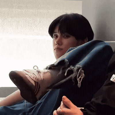 A Person Wearing Ripped Jeans Sits On A Couch With Their Legs Crossed GIF