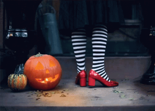 A Person Wearing Striped Socks And Red Heels Standing Next To A Carved Pumpkin GIF