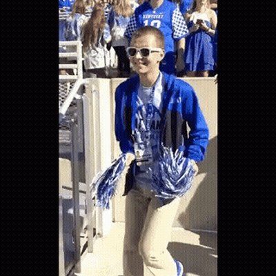 A Person Wearing Sunglasses And A Kentucky Shirt Is Holding Pom Poms While Walking . GIF