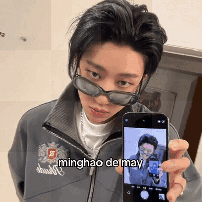A Person Wearing Sunglasses Is Holding Up A Cell Phone With The Name Minghao De May Written On The Screen GIF