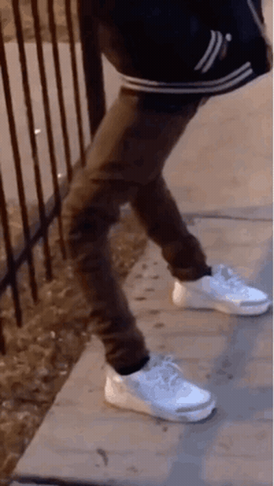 A Person Wearing White Nike Shoes Is Standing On A Sidewalk . GIF