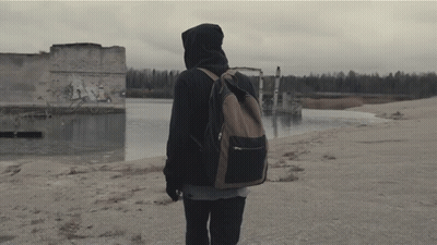 A Person With A Backpack Is Walking On A Beach Near A Body Of Water GIF