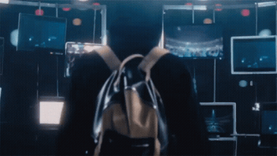 A Person With A Backpack Stands In Front Of A Wall With Monitors GIF
