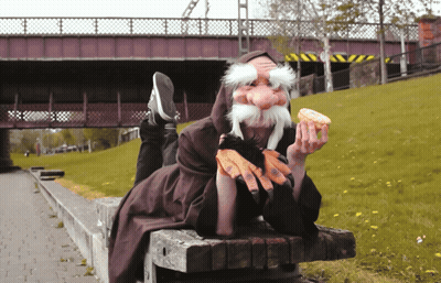 A Person With A Fake Beard Is Eating A Donut On A Bench GIF