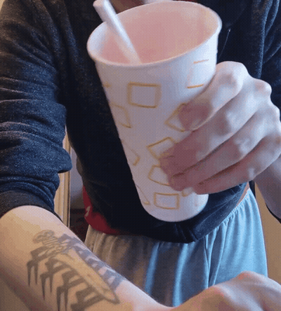 A Person With A Tattoo On Their Arm Holds A Cup With A Straw In It GIF