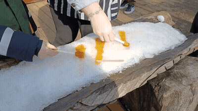 A Person With A Tattoo On Their Arm Is Spreading Maple Syrup On A Pile Of Snow GIF