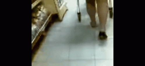 A Person With Crutches Is Walking Down A Tiled Floor In A Store . GIF