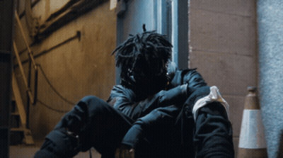 A Person With Dreadlocks Is Sitting On The Ground With Their Head Down GIF