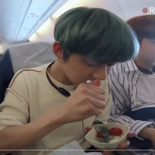 A Person With Green Hair Is Eating A Bowl Of Food On An Airplane GIF