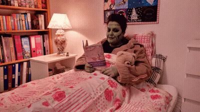 A Person With Green Paint On Their Face Is Reading A Book In A Bed With A Teddy Bear GIF