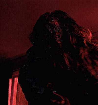 A Person With Long Hair Is Standing In A Dark Room With A Red Light Behind Them GIF