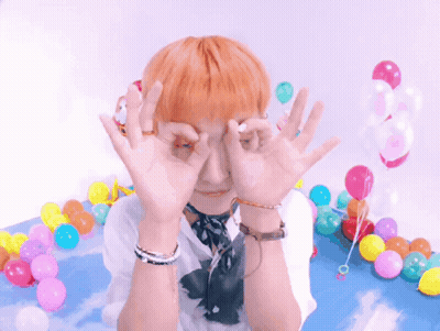 A Person With Orange Hair Covering Their Eyes With Their Hands In Front Of Balloons GIF