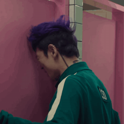 A Person With Purple Hair Leaning Against A Pink Wall GIF