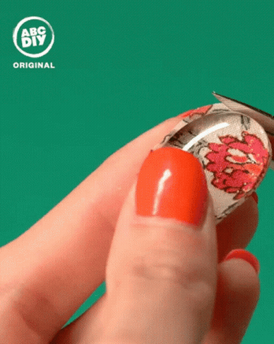 A Person With Red Nails Is Holding A Glass Cabochon With A Floral Design On It In Front Of An Abc Diy Original Logo GIF