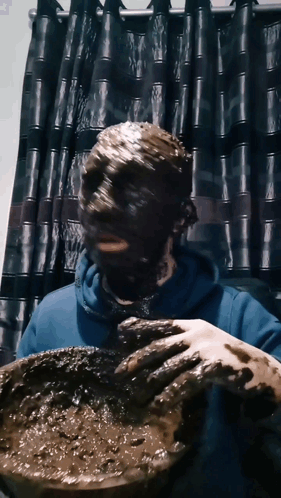 A Person With Their Face Covered In Mud Holds A Bowl GIF
