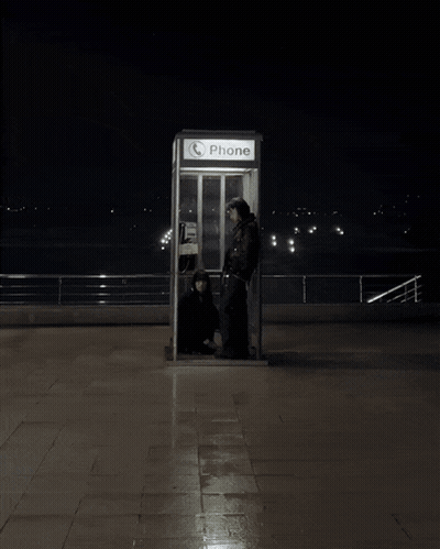 A Phone Booth Is Lit Up At Night With Two People Inside GIF