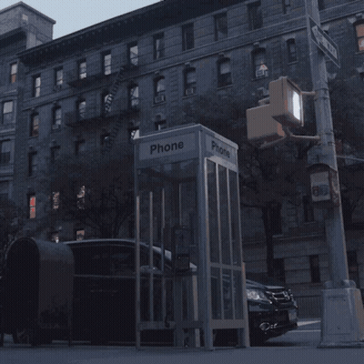 A Phone Booth Sits On The Side Of A Street GIF