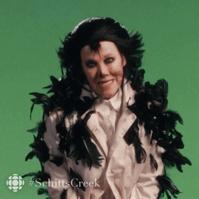 A Picture Of A Woman With Black Feathers Around Her Neck And The Words Schitts Creek GIF