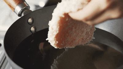 A Piece Of Bread Is Being Poured Into A Pan Of Oil GIF