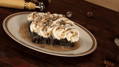 A Piece Of Cake With Whipped Cream And Caramel Sauce On A White Plate GIF