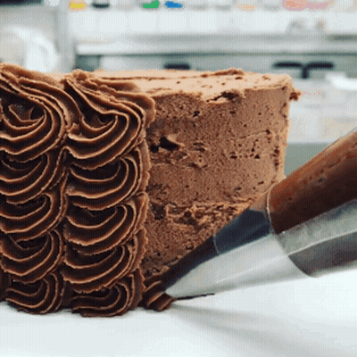 A Piece Of Chocolate Cake Is Being Frosted By A Piping Nozzle GIF