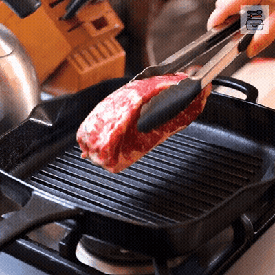A Piece Of Meat Is Being Cooked In A Pan With Tongs GIF