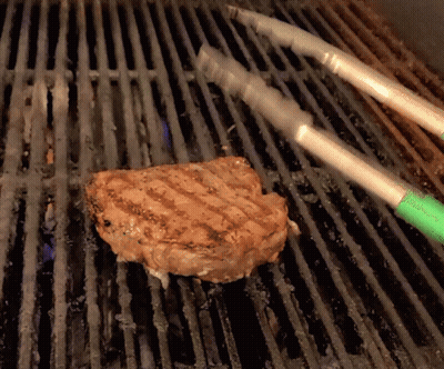 A Piece Of Meat Is Being Cooked On A Grill With Tongs GIF