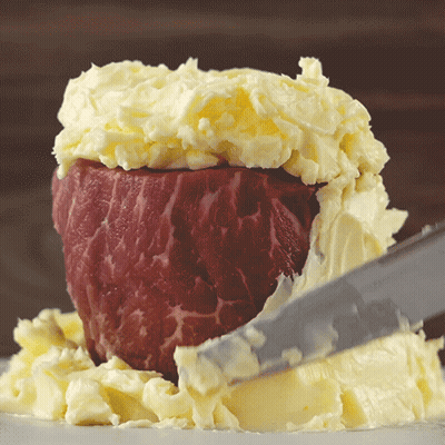 A Piece Of Meat Is Covered In Butter And Being Sliced By A Knife GIF