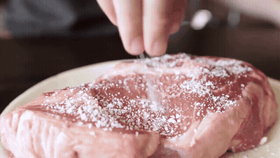 A Piece Of Raw Meat Is Being Seasoned With Salt GIF