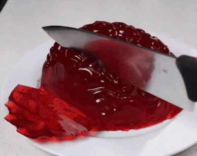 A Piece Of Red Jelly Is Being Cut With A Knife On A White Plate GIF