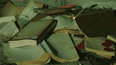 A Pile Of Books Are On Fire And One Of Them Has A Barcode GIF