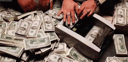 A Pile Of Money Is Sitting On A Table And A Person Is Taking Money Out Of A Box . GIF