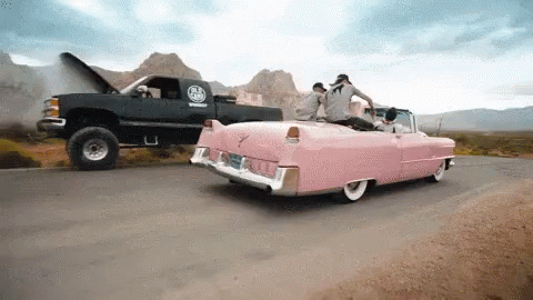 A Pink Car Is Being Towed By A Black Truck With The Hood Up GIF