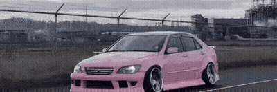 a pink car is driving down a road next to a chain link fence .